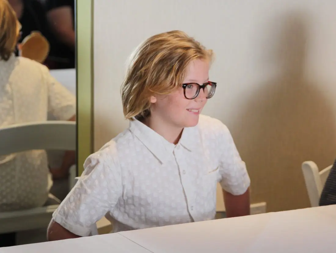 Incredibles 2 Interview with Huck Milner sitting at table. Voice actors of Dash and Violet Parr Tell All in this revealing exclusive interview.