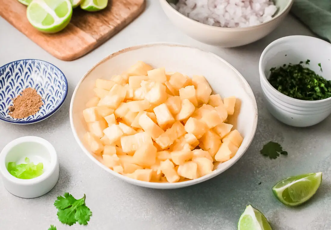 Ingredients shot for pineapple salsa dip. Featuring a bowl on sliced pineapple, limes, red onions, jalapenos, and taco seasoning.