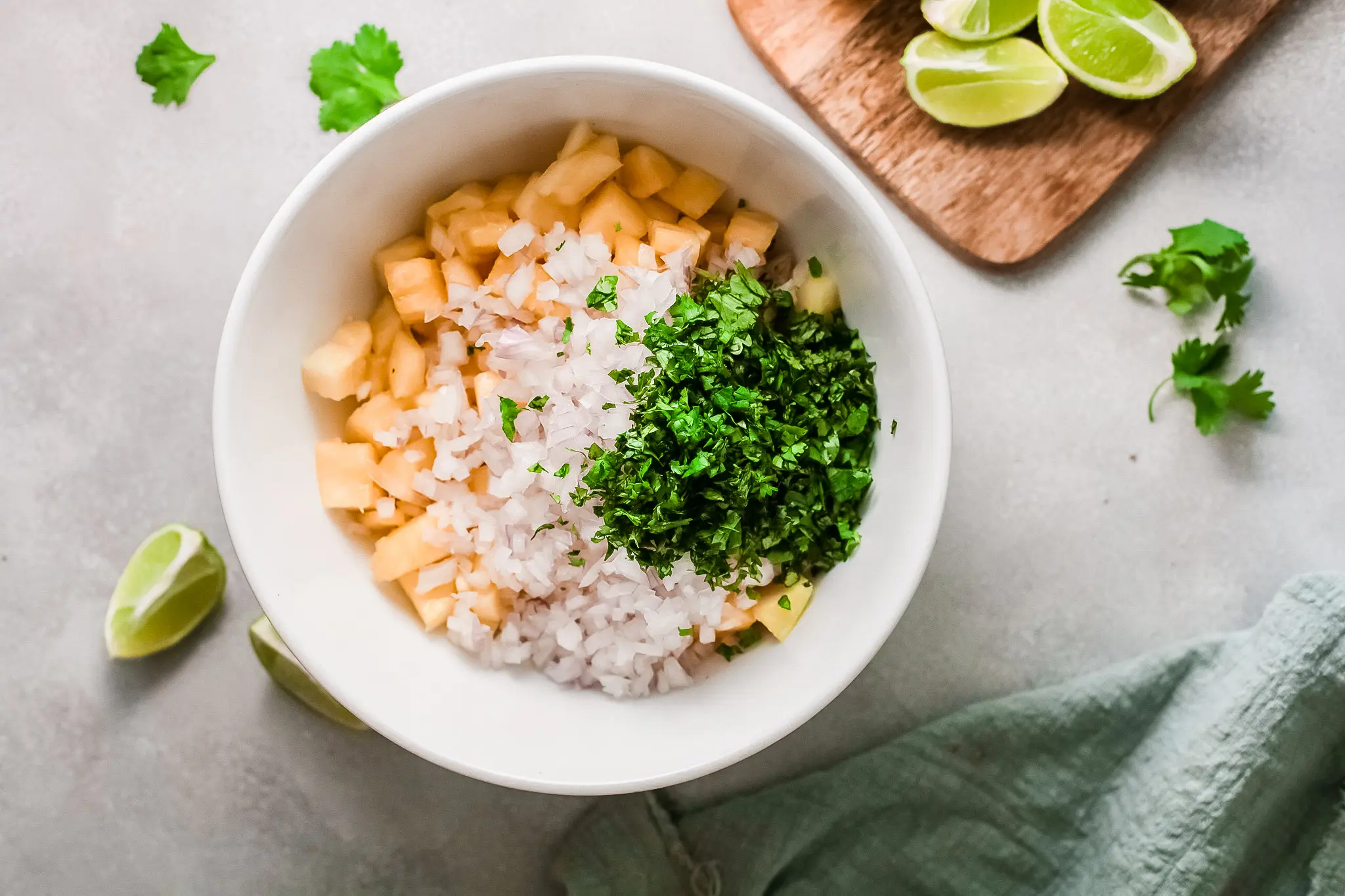 All of the ingredients in bowl for pineapple salsa dip. Featuring a bowl on sliced pineapple, limes, red onions, jalapenos, and taco seasoning.