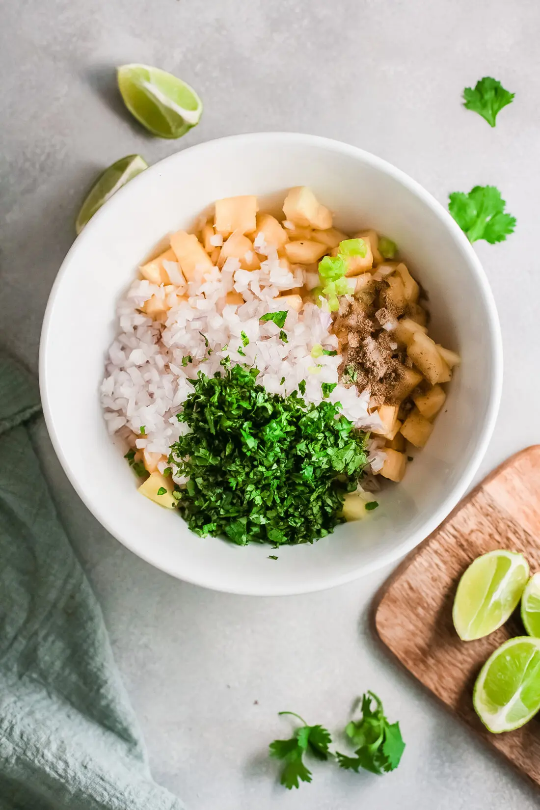 All ingredients in bowl for pineapple salsa dip. Featuring a bowl on sliced pineapple, limes, red onions, jalapenos, and taco seasoning.